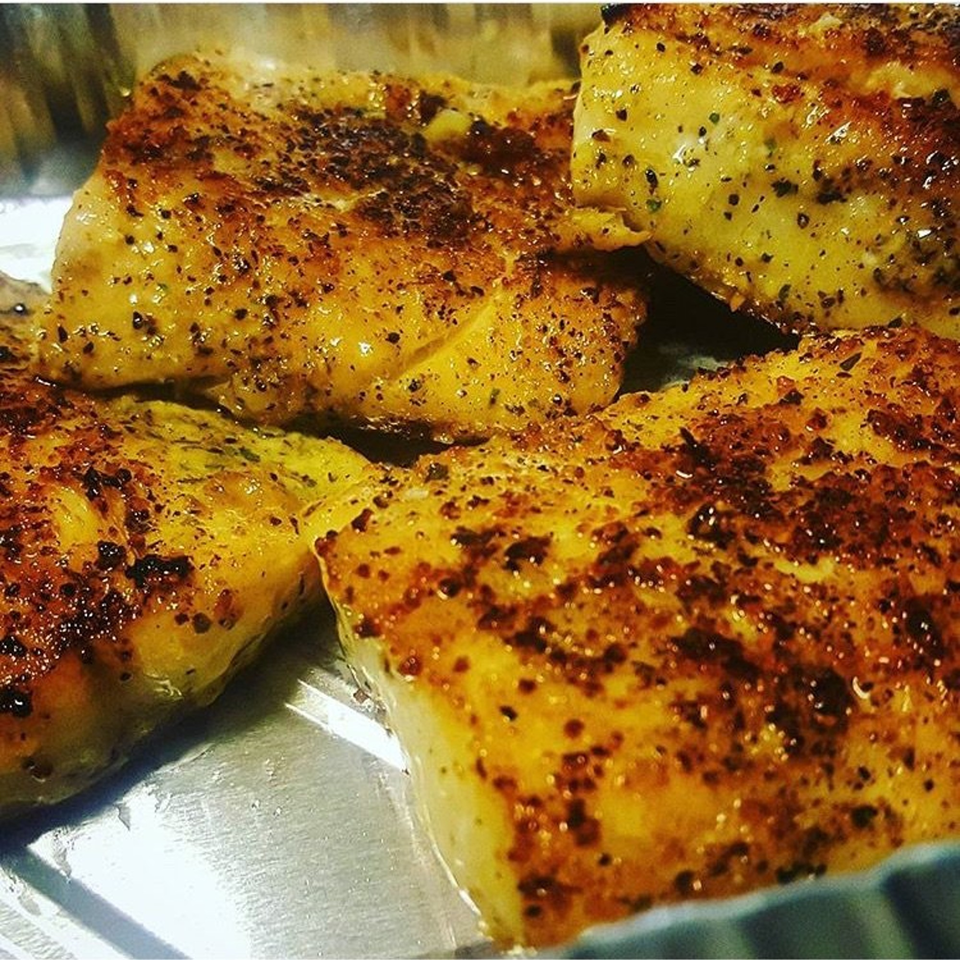 Close-up of four pieces of golden-brown, seasoned fish fillets in a metal pan.