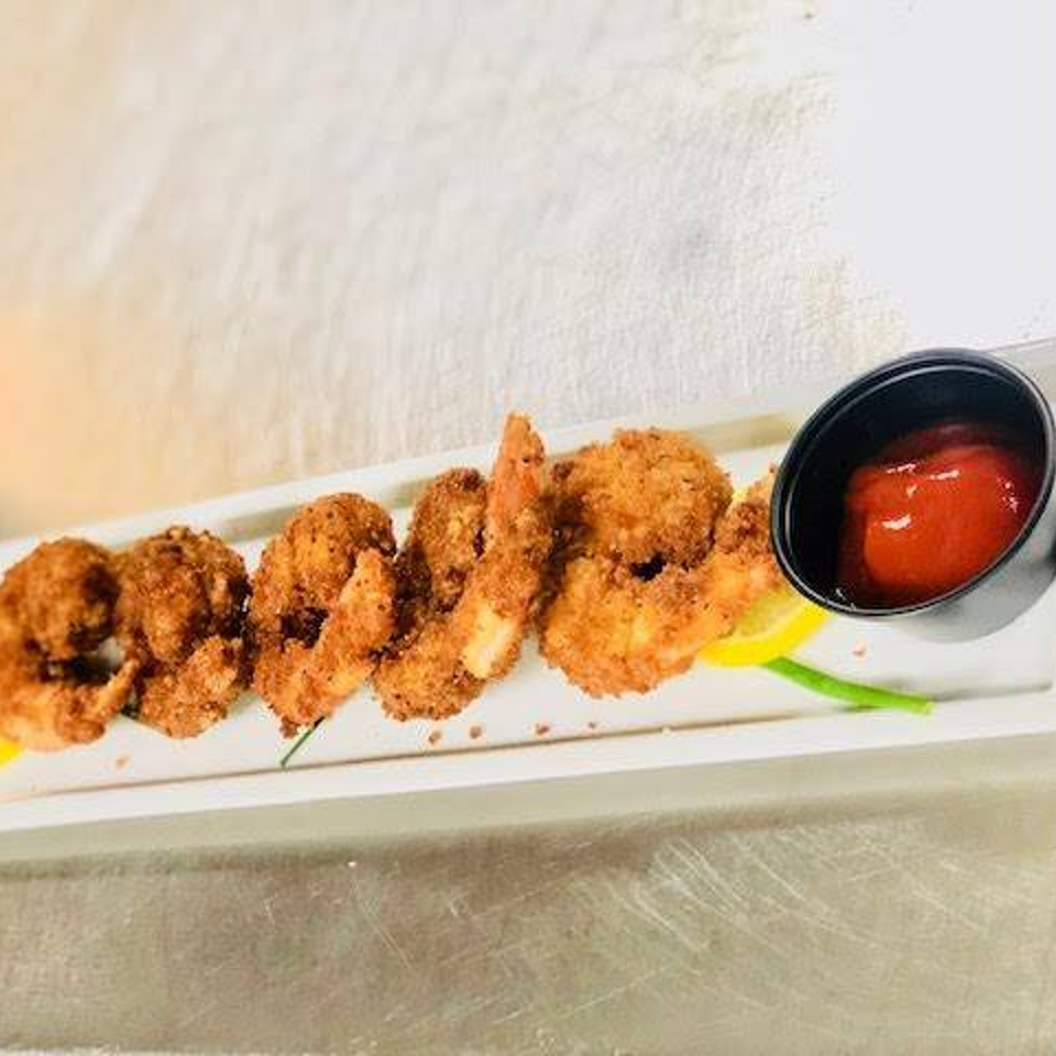 Crispy fried shrimp with lemon wedges and a side of ketchup on a white rectangular plate.