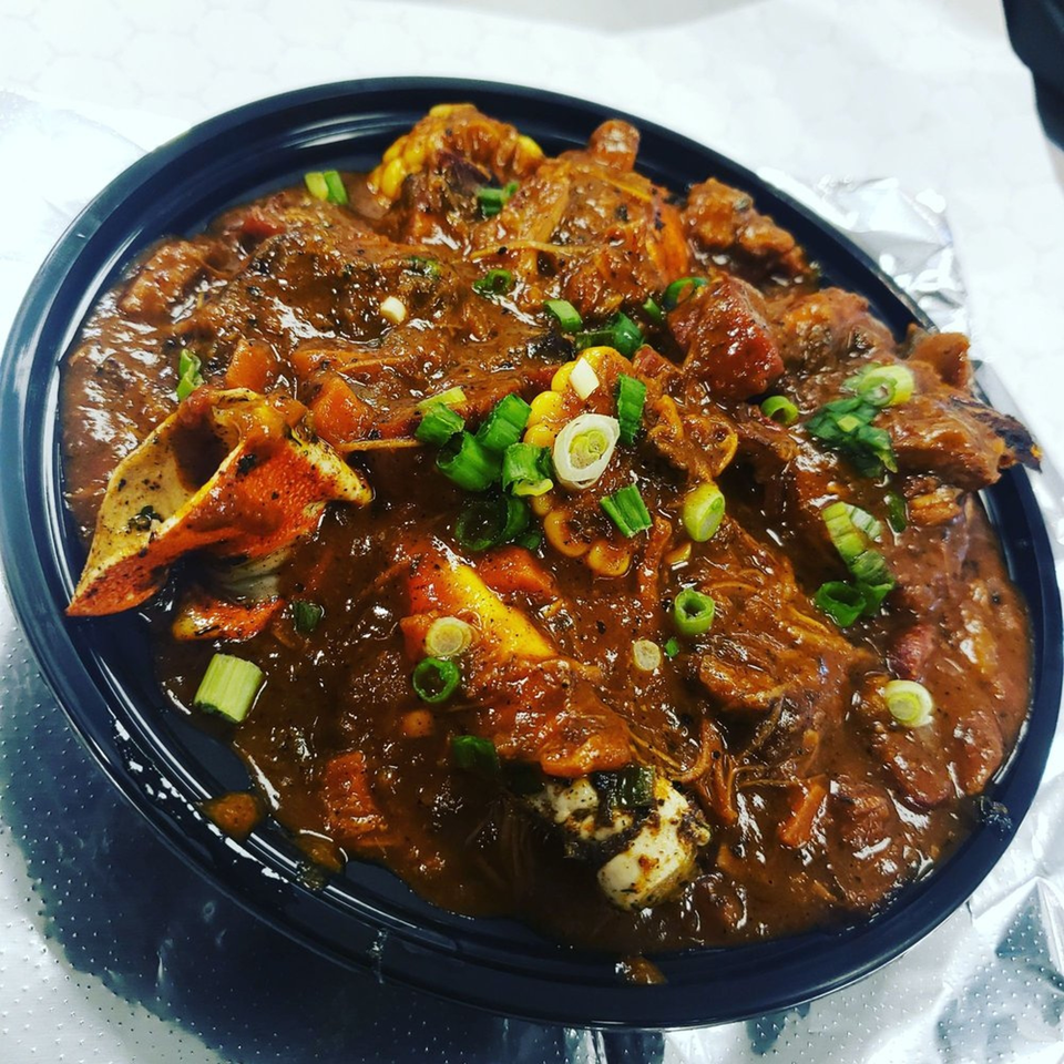 A dark stew with crab claws, corn, and green onions in a black bowl.